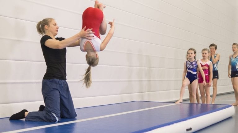 Teacher helping gymnast with sommersault